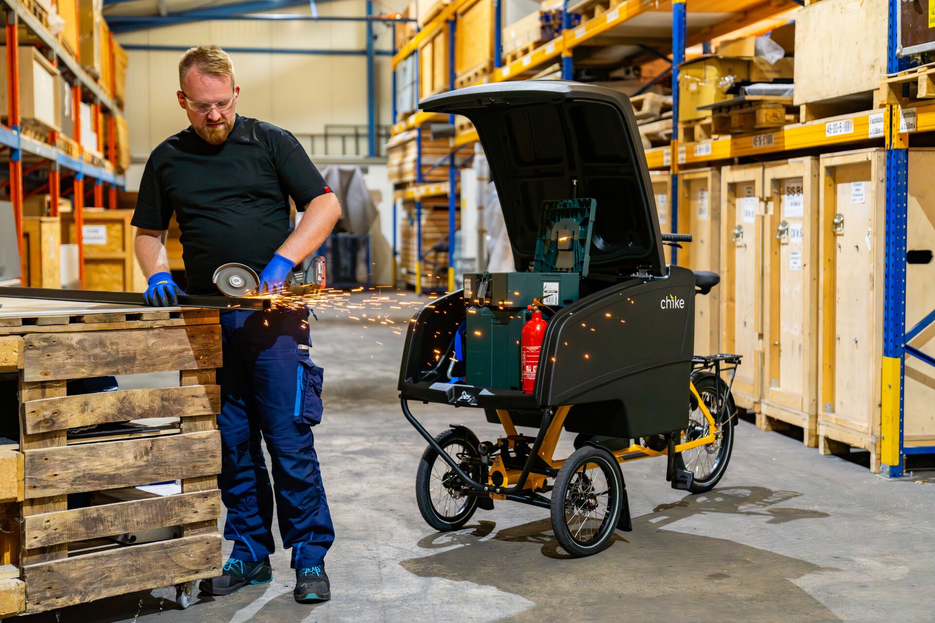 chike E‑Cargo Pro Lastenrad in Schwarz mit geoeffnetem Laderaum in Werkstattszene.