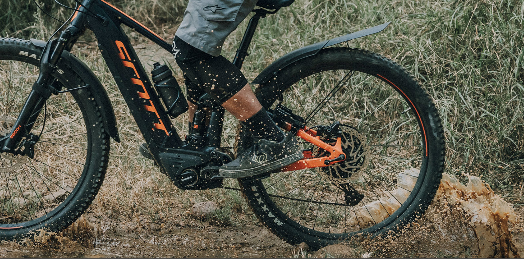 E-Mountainbike mit montiertem Topeak TetraFender M1 fährt durch schlammiges Gelände, Wasser spritzt vom Reifen.