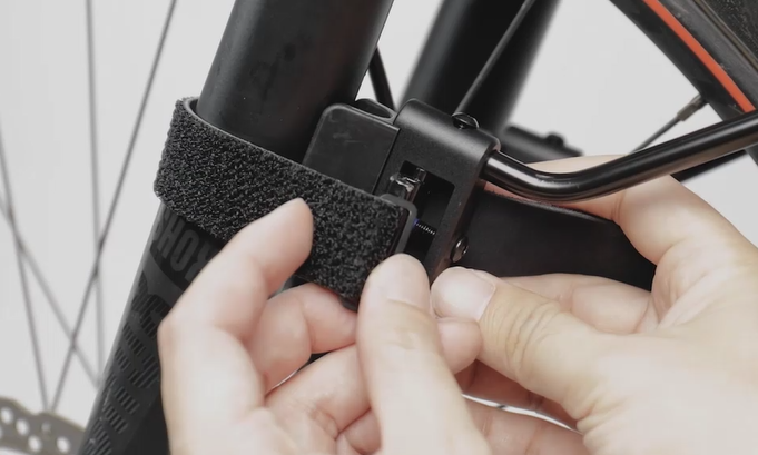  Detailaufnahme der Montage des Topeak TetraFender M1, Hände befestigen Klettgurt an der Fahrradgabel.