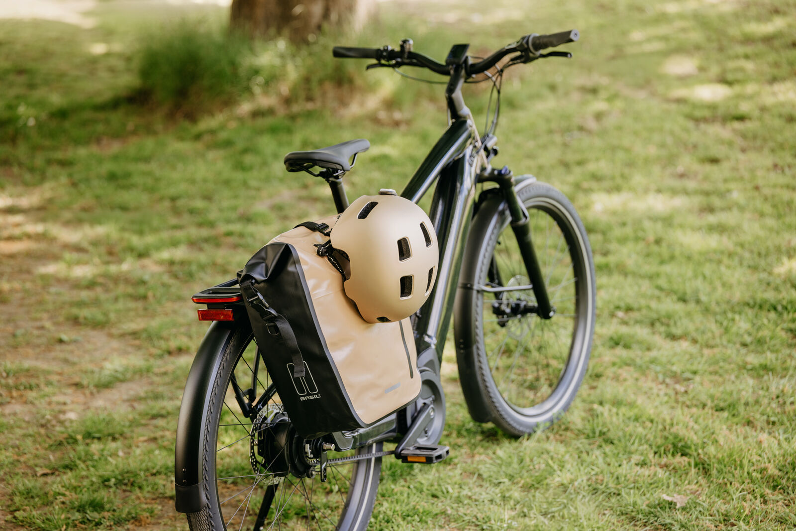 Basil Rivo L Fahrradtasche in Beige und Schwarz, montiert an einem Fahrrad-Gepäckträger, mit befestigtem Helm.