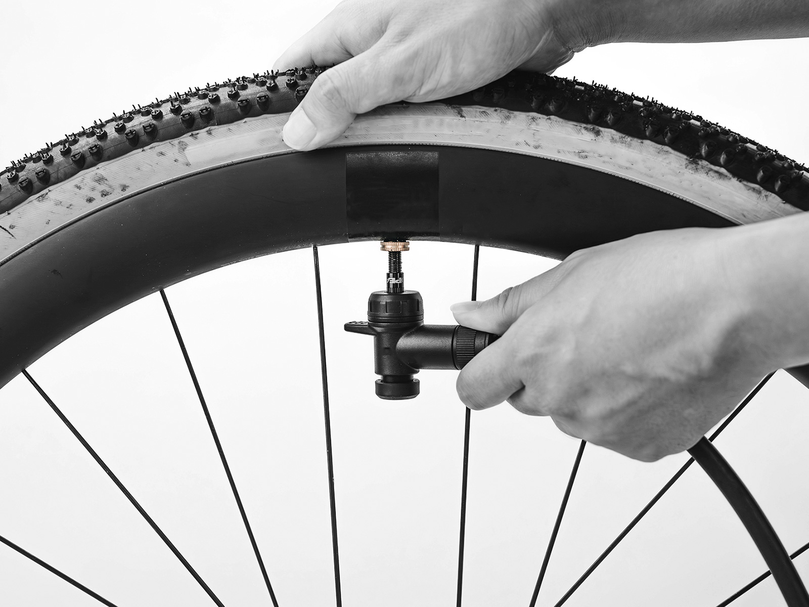 Schwarz-weiß-Foto von Händen, die einen RapidHead-Pumpenkopf an ein Tubeless-Ventil eines Gravelbike-Reifens anschließen, seitliche Ansicht.