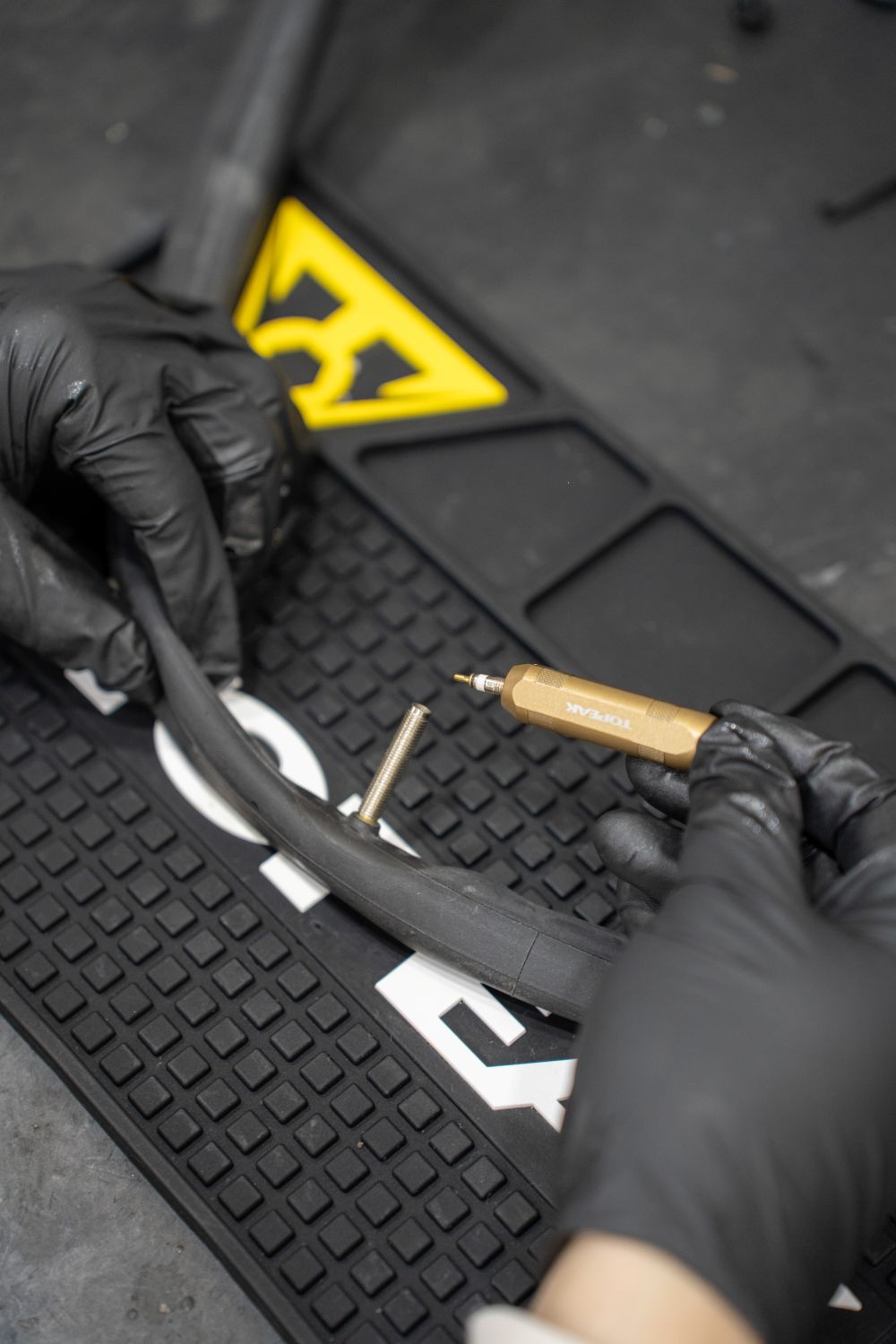 Anwendung des Topeak Ventil-Werkzeugs Team Issue beim Entfernen eines Ventileinsatzes aus einem Fahrradschlauch auf Topeak-Werkstattmatte.