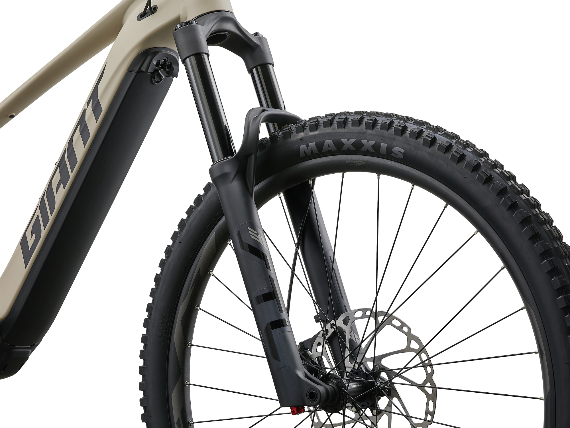 Giant Stance E+ E‑MTB in Almond mit Federgabel und Maxxis‑Reifen in Front‑Detailansicht.